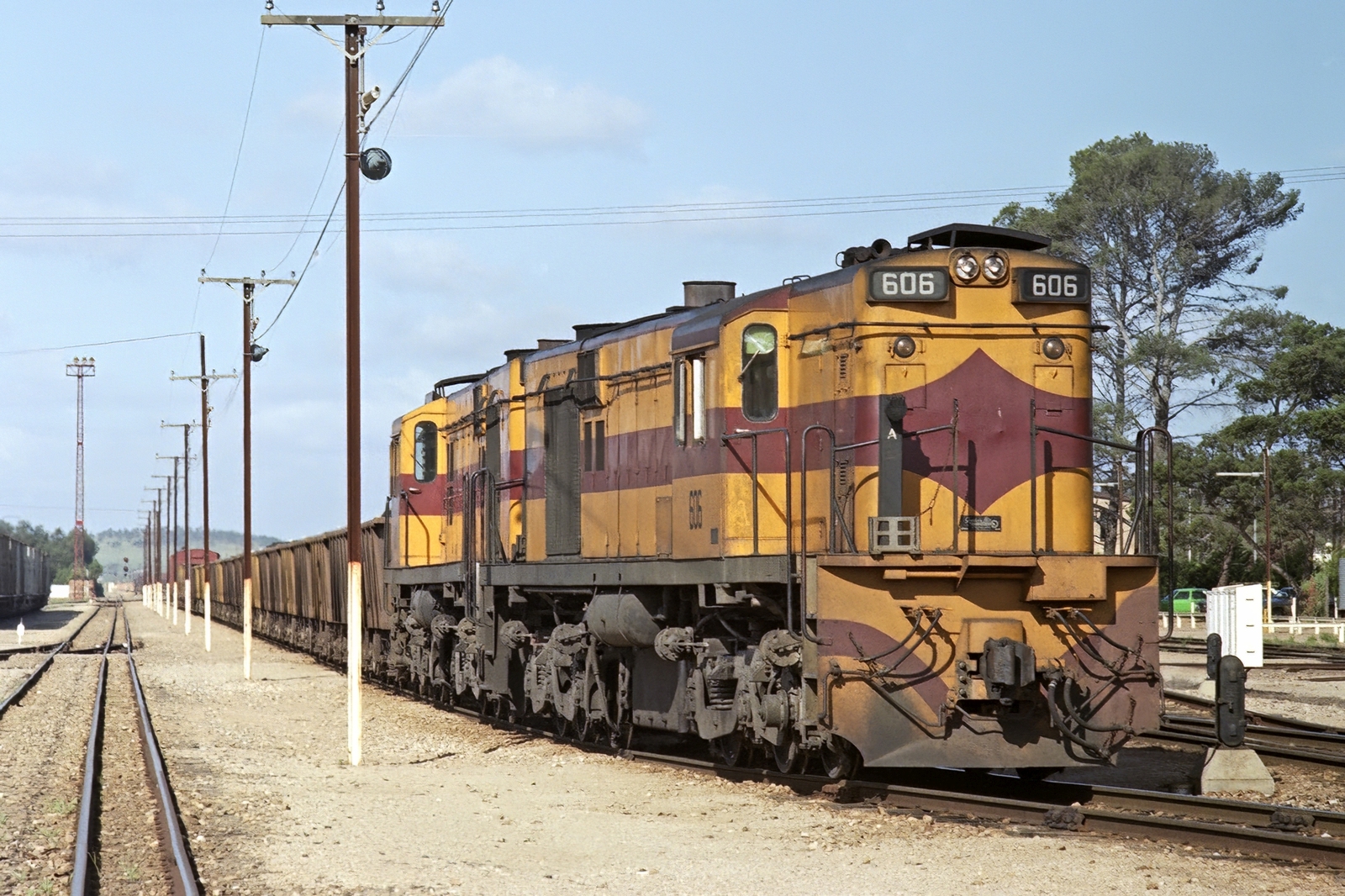 An image showing 600 class diesel locomotives 606 and 600 in yellow and maroon livery on track hauling open wagons. Shot taken during the day.